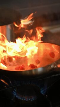 Closeup of a pan with frying ingredients in flames. Cook flipping ingredients in a pan with fire flare on a gas stove in a restaurant kitchen. Beautiful flames in a pan on a new modern kitchen.