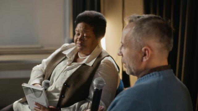 Middle-aged African American woman and middle-aged Caucasian man speaking into microphones during book presentation. Perfect for corporate communication and educational event marketing