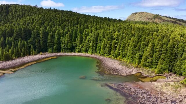 Aerial drone footage showcasing the emerald waters of Canario Lagoon bordered by dense evergreen forest in Sao Miguel Azores Portugal Europe on a sunny day