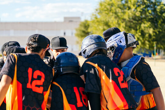 Youth baseball team players and coach gathering in a huddle, discussing game strategy and teamwork during a practice session