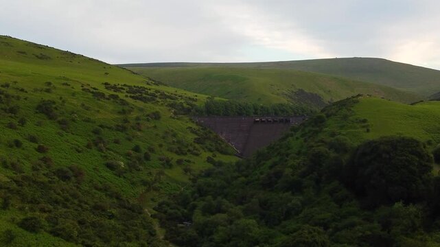 Steep grassy hills close in around Meldon Dam as a drone glides along the narrow wooded gorge on Dartmoor.