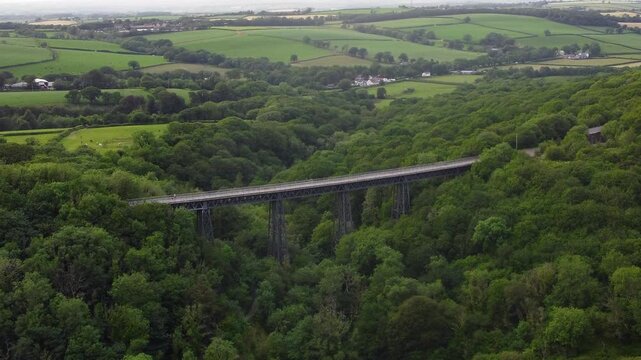 Historic Meldon Viaduct cuts through dense summer woodland with patchwork Devon farmland in the distance.