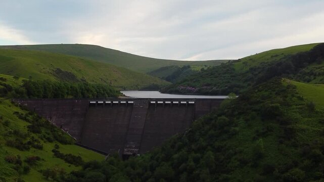 Meldon Dam spans a deep Dartmoor valley with Meldon Reservoir backed by rolling green hills under a soft evening sky.