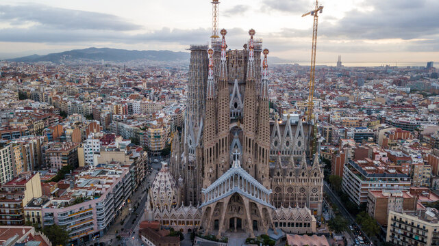 Aerial view of the Sagrada Familia basilica under construction with towering spires and cranes, surrounded by the dense urban landscape of Barcelona, Catalonia, Spain.