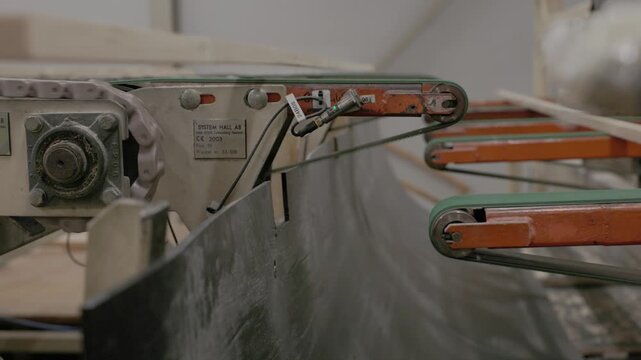 Fresh wooden boards travel across metal rollers and chain conveyors inside a lumber processing facility