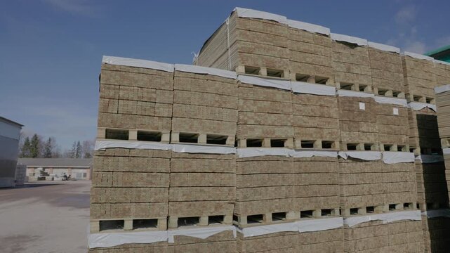 Large bundles of cut wooden boards are stacked on pallets outdoors under a blue sky, ready for storage, shipping, or construction supply