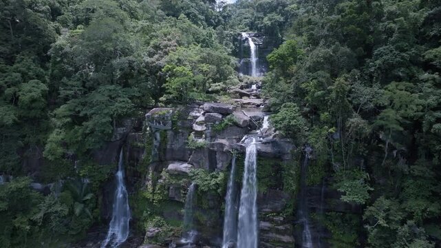 A drone flying over a waterfall in a deep green forest provides an aerial, top-down view of a National Park in Laos PDR.