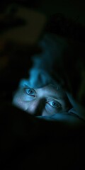 Obraz premium Person lying in bed with blue smartphone light on face in dark bedroom, digital insomnia concept, copy space
