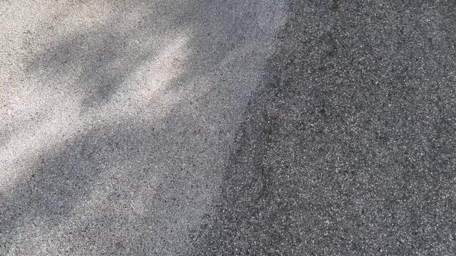 Superficie asfaltata con contrasto tra zona chiara illuminata dal sole e area scura in ombra