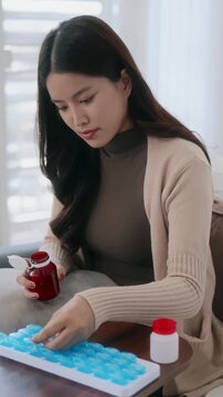 Asian woman organizing pills in a pill box for preparing daily routine medication