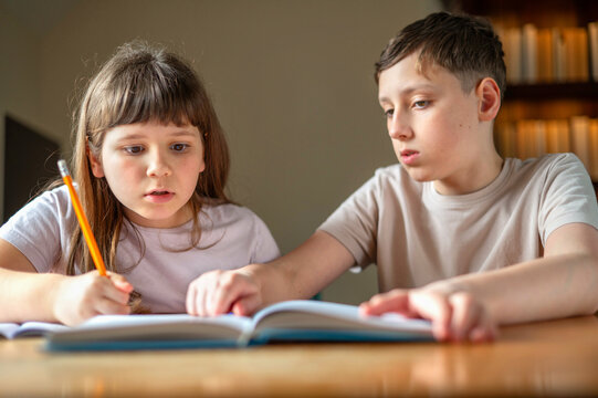 Brother helping sister study with textbook at home