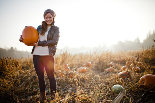Happy woman holding a big pumpkin in a patch