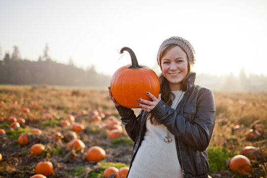 Smiling young woman holding a pumpkin in a patch