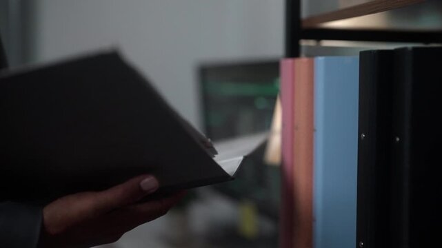 Professional close-up video of an employee organizing file binders on an office shelf. Suitable for themes of office administration, document storage, corporate records, business organization, product