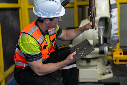 Industrial Robot Technician: A male technician in a hard hat and safety vest supervises an industrial robotic arm in a factory setting, emphasizing precision engineering and automation.