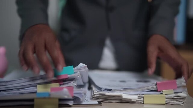 Close-up video of hands reviewing business files and organized office documents at a workstation. Perfect for illustrating office workflow, document processing, corporate administration, record manage