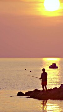 Person silhouette fishing from sea shore at sunset