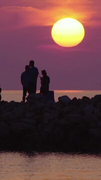 Silhouette of family with kids fishing at sunset with big orange sun