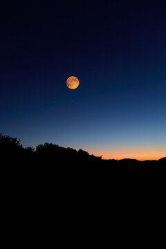 Full Moon on a twilight sky with countryside silhouettes.