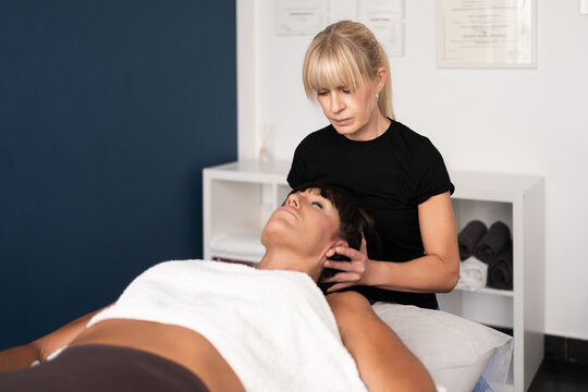 Female therapist performing gentle neck mobilization on relaxed adult patient in bright clinical treatment room with modern decor, conveying careful hands-on care and recovery support