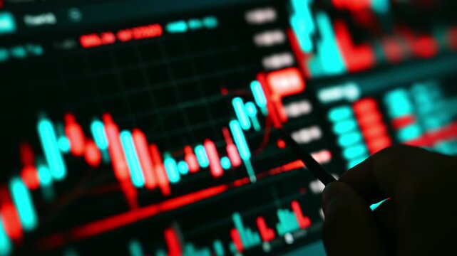 Businessperson holding a stylus pen while analyzing red and blue stock candlestick charts on a digital trading screen, representing market analysis, investment, fintech, and financial decision making.