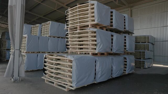 Large strapped stacks of wooden boards stored on pallets in an industrial warehouse. Copyright: no people or visible logos; property release may be needed