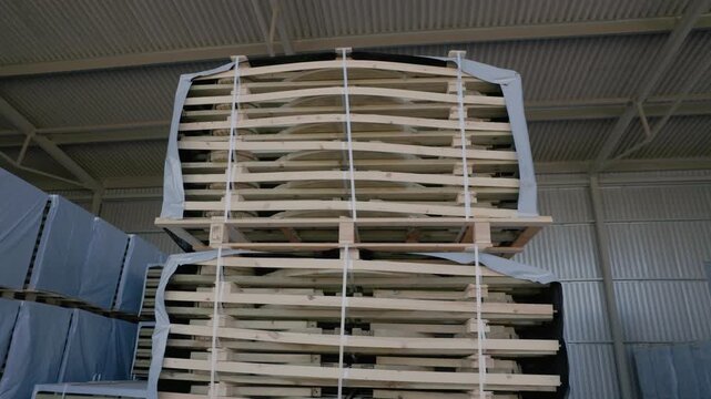 Large strapped stacks of wooden boards stored on pallets in an industrial warehouse. Copyright: no people or visible logos; property release may be needed