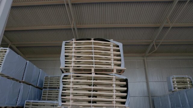 Large strapped stacks of wooden boards stored on pallets in an industrial warehouse. Copyright: no people or visible logos; property release may be needed