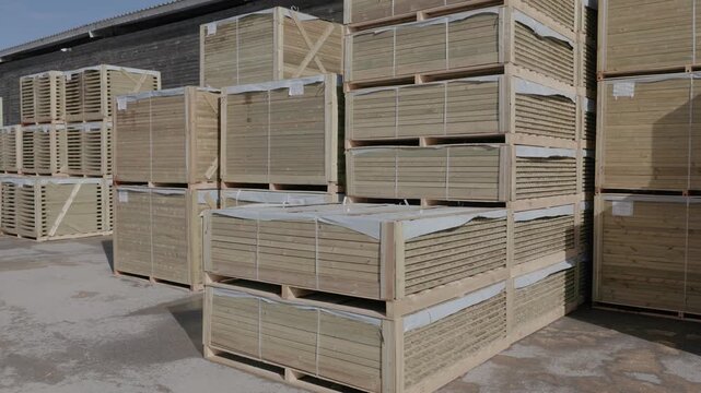Bundled wooden boards stacked outside a warehouse under clear sky. Copyright: no people or visible logos; property release may be needed
