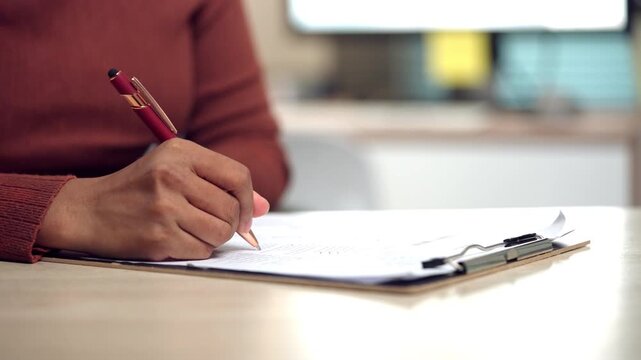 Close-up of a woman completing and signing a legal agreement form on a clipboard. Perfect for illustrating contracts, administrative paperwork, business transactions, and official approval processes.