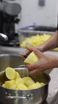 Hands peeling a raw potato with a knife over a pot of peeled potatoes