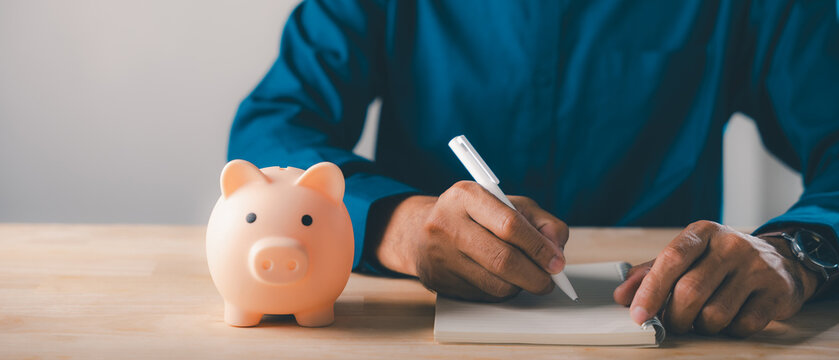 Piggy bank saving for learning education college and career growth, man writing finance plan in notebook on wooden desk, investment for tuition fees and professional development