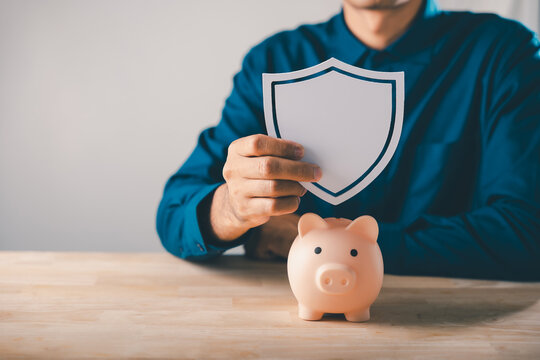 Man holds shield over piggy bank to protect money, save and plan, financial finance insurance saving ensures security, long term capital investment and sustainable wealth growth