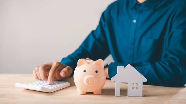 Man calculates real estate investment budget, saving money in piggy bank for home property insurance, planning financial strategy for buying new residential house model