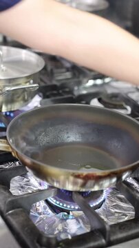 Chicken pieces cooking in a frying pan over a blue gas flame on the stove