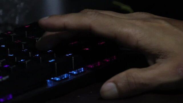 A close up of a person's hand typing on a backlit mechanical RGB gaming keyboard