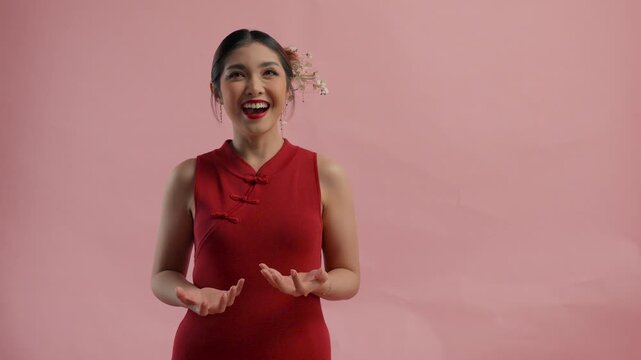 Excited young Asian woman is throwing angpao or red packet monetary gift, isolated by pink background.