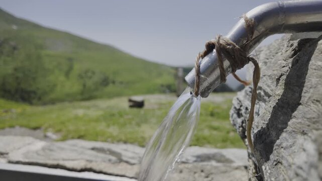 Fresh, clean drinking water pouring from a rustic metal spout set in a stone trough, providing a vital resource for livestock in the high alpine meadows of the Pyrenees mountains in Catalonia