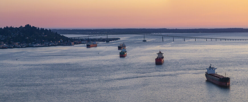 Aerial view of the Columbia River with cargo ships navigating the waterway near the Astoria-Megler Bridge at sunset in Astoria, Oregon, United States.