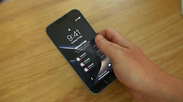 Missed calls from a University appear on a smartphone lock screen while a person holds the device above a wooden table indoors. Mobile notifications emphasize higher education communication, admission