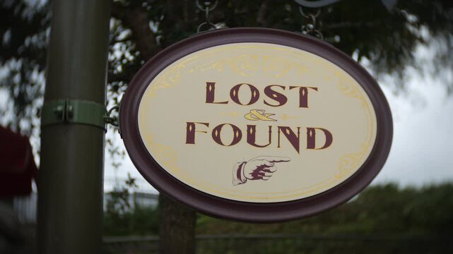 Lost and Found sign hanging outdoors with decorative lettering and a pointing hand symbol in a close-up shot. Public services, visitor assistance, and misplaced property collection are clearly emphasi