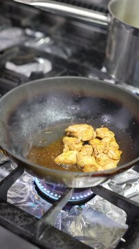 Chicken pieces cooking in a frying pan over a blue gas flame on the stove