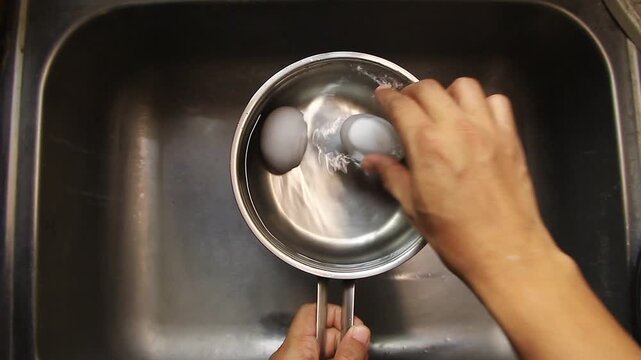 Hand putting eggs in a pan with water.
