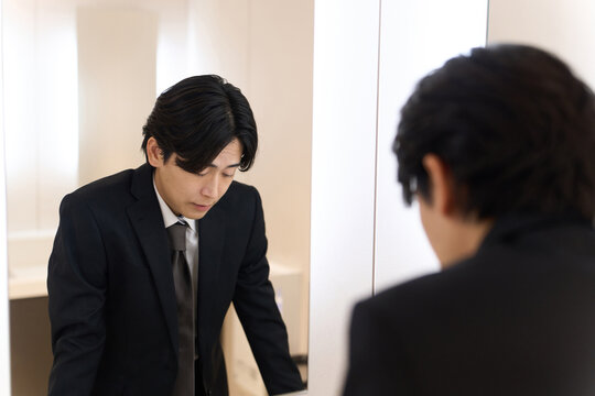 トイレの鏡で表情のチェックをするアジア人男性