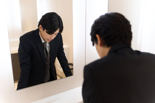 トイレの鏡で表情のチェックをするアジア人男性