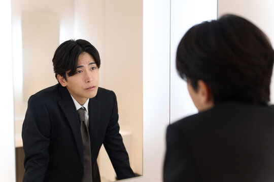 トイレの鏡で表情のチェックをするアジア人男性