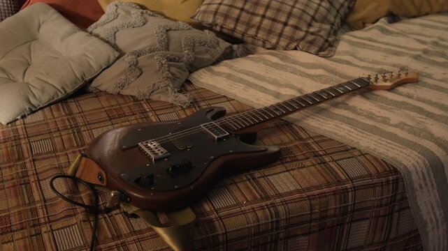 Electric guitar lying on plaid bedspread with pillows in bedroom. Footage for music education, hobbyist lifestyle, or creative arts marketing campaigns