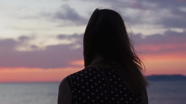 Rear view silhouette of a young woman in a polka dot dress looking at the beautiful sea sunset