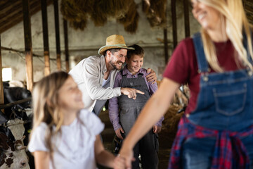 Obraz premium Happy father teaching son about livestock in a barn, with other family members present, highlighting rural lifestyle and upbringing
