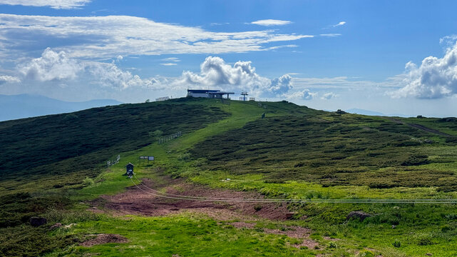 Grassy hilltop with a summit shelter under soft daylight clouds, lone hiker on path, suitable for travel blogs, landscape editorials, tourism marketing,  Babin Zub Serbia